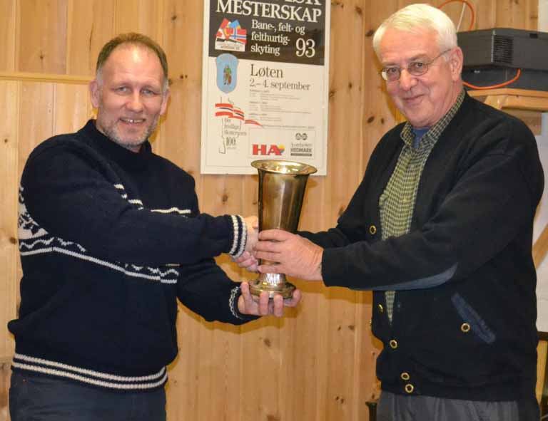 På bildet ser vi Bjørn Karlsen (til venstre) som på vegne av familien overleverer den store sølvpokalen som settes opp på Ola Karlsens minnestevne. Formannen Henry Nordvi tar i mot den 30 cm høye sølvpokalen. Det var kona Beret Karlsen som satte opp denne pokalen som minnepokal etter sin mann Ola Karlsen
